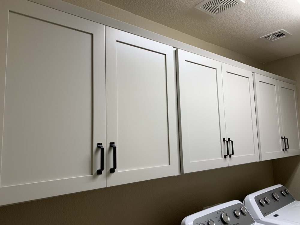 White shaker upper cabinets with black pulls installed above laundry machines